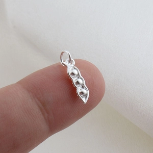 Macro detail of silver three-bead pea pod pendant showing scale against a finger