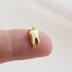 Close-up of a mini gold-plated tooth pendant held by hand for DIY jewelry making