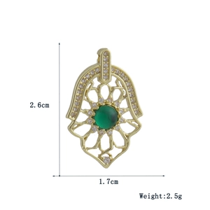 Detailed view of a gold Hamsa hand pendant with sparkling zircons and a green center stone