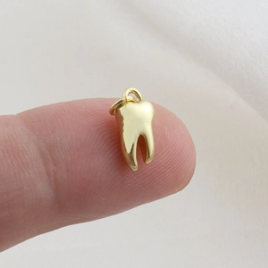 Macro shot of a tiny gold tooth pendant on a fingertip showing realistic micro scale