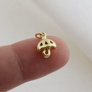 Macro shot of a small gold umbrella pendant with hollow triangle details on a fingertip