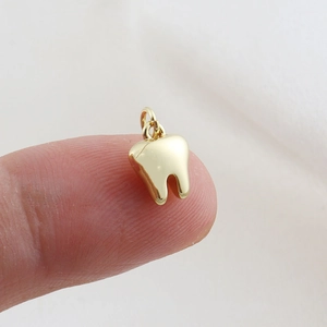 Close-up of a small golden tooth-shaped charm with a metal ring on a fingertip
