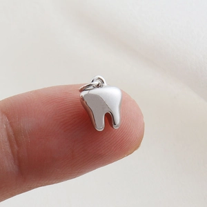 Close-up of a polished tooth-shaped silver charm on a fingertip for size reference