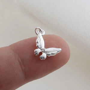 Detail of silver butterfly charm with textured wings and zircon stone held on fingertip