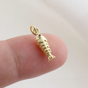 Macro detail of a small gold fish charm with scale texture and black stone eye on fingertip