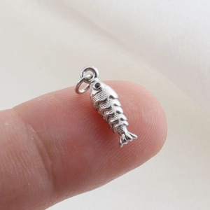 Macro shot of a fish-shaped silver metal pendant with fine scales on a white fabric background