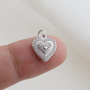 Dettaglio di un ciondolo a cuore in argento con pavé di zirconi su un dito