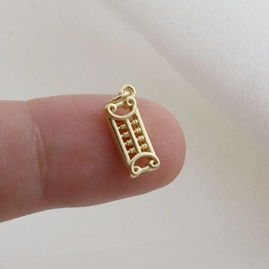 Miniature golden abacus pendant charm shown on a fingertip for size perspective