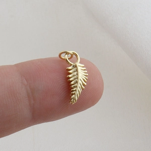 Delicate gold feather pendant charm with fine leaf texture held by hand for size scaling