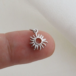 Macro di piccolo ciondolo a sole in argento sul polpastrello per dettagli dimensioni