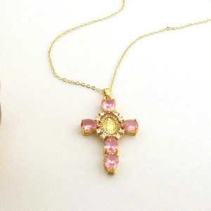 Detailed view of a golden cross pendant with pink gemstones and religious emblem