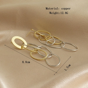 Détail de boucles d'oreilles pendantes en cuivre doré de 8,8 cm sur fond de soie