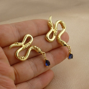 Détail de boucles d'oreilles serpent dorées avec pierre bleue sur du velours