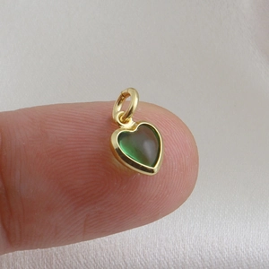 Λεπτομέρεια από ένα μικρό πράσινο μενταγιόν καρδιά με επιχρύσωση 18 καρατίων σε δάχτυλο