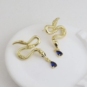 Boucles d'oreilles serpent dorées avec gouttes en cristal bleu sur plateau blanc
