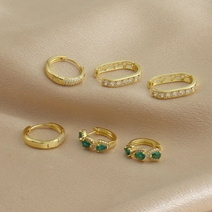 Détail de créoles dorées serties de diamants pavés et de pierres vertes sur de la soie