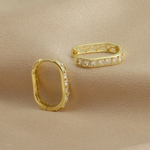 Détail de boucles d'oreilles rectangulaires dorées avec zircons sur fond de satin