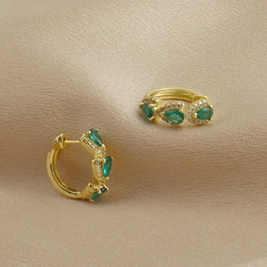 Détail de boucles d'oreilles dorées avec pierres vertes en poire et halo de zircons blancs