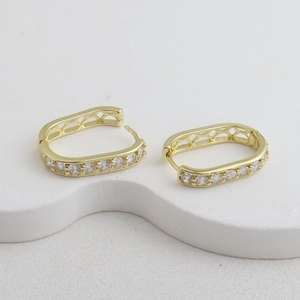 Détail de boucles d'oreilles dorées rectangulaires avec zircons et motif en maille ajourée