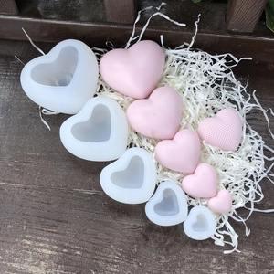 Macro shot of 3D heart silicone molds and pink handmade candles on a dark wood table