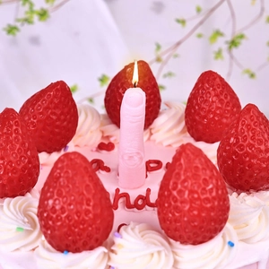Pink finger-shaped novelty candle burning on top of a strawberry cream cake decoration