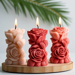Three lit rose column scented candles on a round wooden tray with palm leaf decor
