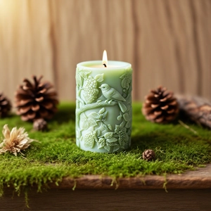 Embossed bird and floral pattern pillar candle on moss with a warm flickering flame
