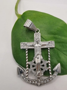 Macro shot of silver anchor cross pendant with Jesus relief and white crystals on green leaf
