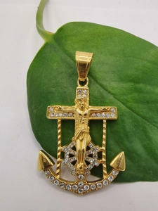 Macro shot of gold-plated anchor cross pendant with white rhinestones on green leaves