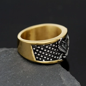 Macro detail of bicolored stainless steel eagle ring on a dark stone background