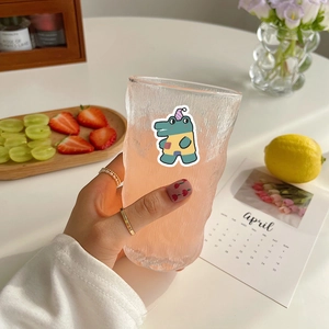 Cute cartoon dinosaur sticker on a textured glass cup held in a bright lifestyle setting