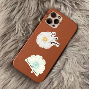 Brown leather iPhone case with daisy patterns and artistic typography in a flat lay view