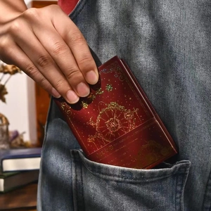 Pocket-sized wine red Book of Answers with gold foil stars being pulled from a denim pocket