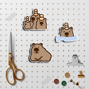 Three cute cartoon capybara stickers set on a pegboard with decorative stationery