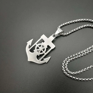 Macro view of gold-plated anchor pendant with ship wheel cutout on brushed steel chain