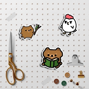 Detail of cute bear and chick cartoon stickers on a white pegboard with gold scissors