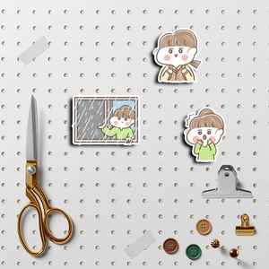 Macro detail of three cartoon girl stickers on a pegboard with stationery accessories