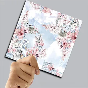 Close-up of hand holding a square vintage spring garden scrapbook paper with floral bird motifs