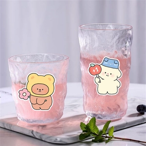 Set of two textured glass cups with cute bear and dog stickers on marble stand