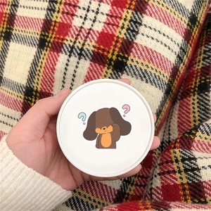 Close-up of hand holding a cute cartoon dog sticker on a white round cosmetic case cover