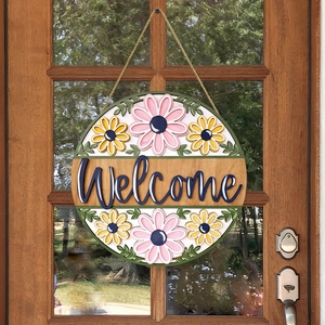 Floral welcome wood hanging sign with 3D letters and daisy patterns on a glass door
