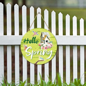 Round wooden Hello Spring sign with colorful birds and flowers on a white fence