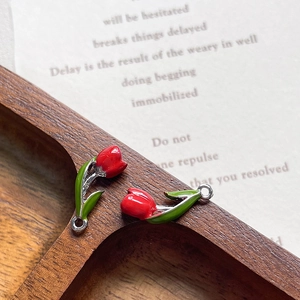 Macro view of 2 red tulip alloy charms on a wooden tray for DIY jewelry making