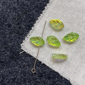 Macro shot of green glass leaf beads with iridescent gold coating and detailed vein texture