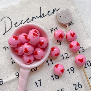 Close-up of pink round acrylic beads with red heart patterns for DIY jewelry making