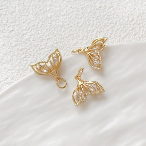 Macro shot of three gold fishtail pendants with clear zircons on a white ceramic plate