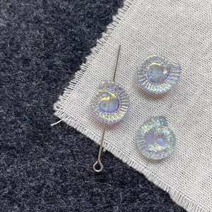 Iridescent ammonite glass beads for DIY jewelry with silver pin on a textured background
