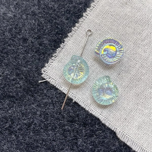 Macro detail of iridescent snail-shaped glass beads for DIY jewelry with silver pins