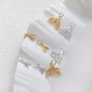 Macro detail of zircon mermaid tail pendants in gold and silver on white tray
