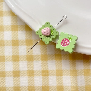 Macro view of green cookie-shaped beads with pink strawberry and sweet engraving
